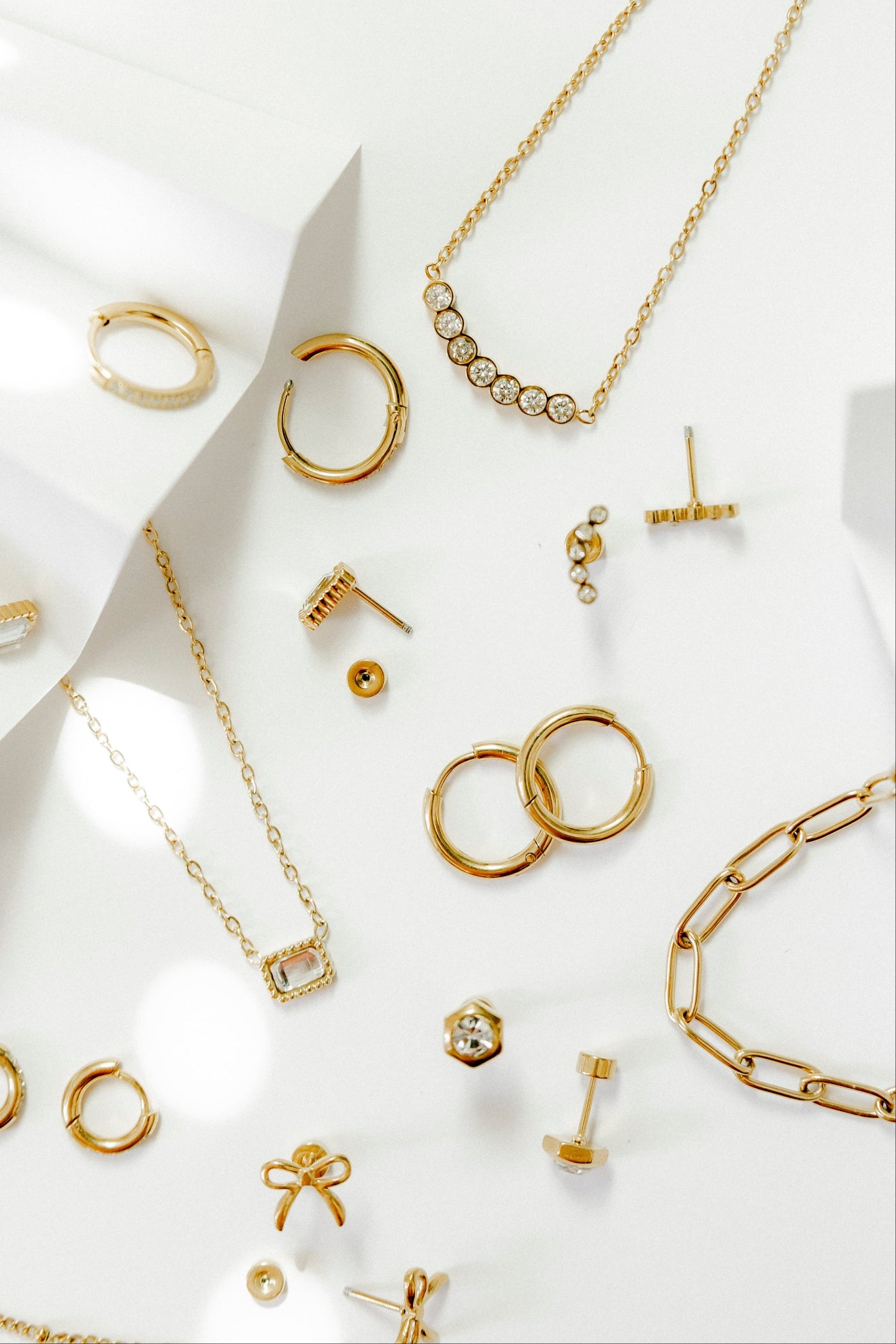 Linny co Flatback stud earrings and hypoallergenic necklaces. Gold jewelry including rings, necklaces, and earrings on a white fabric background