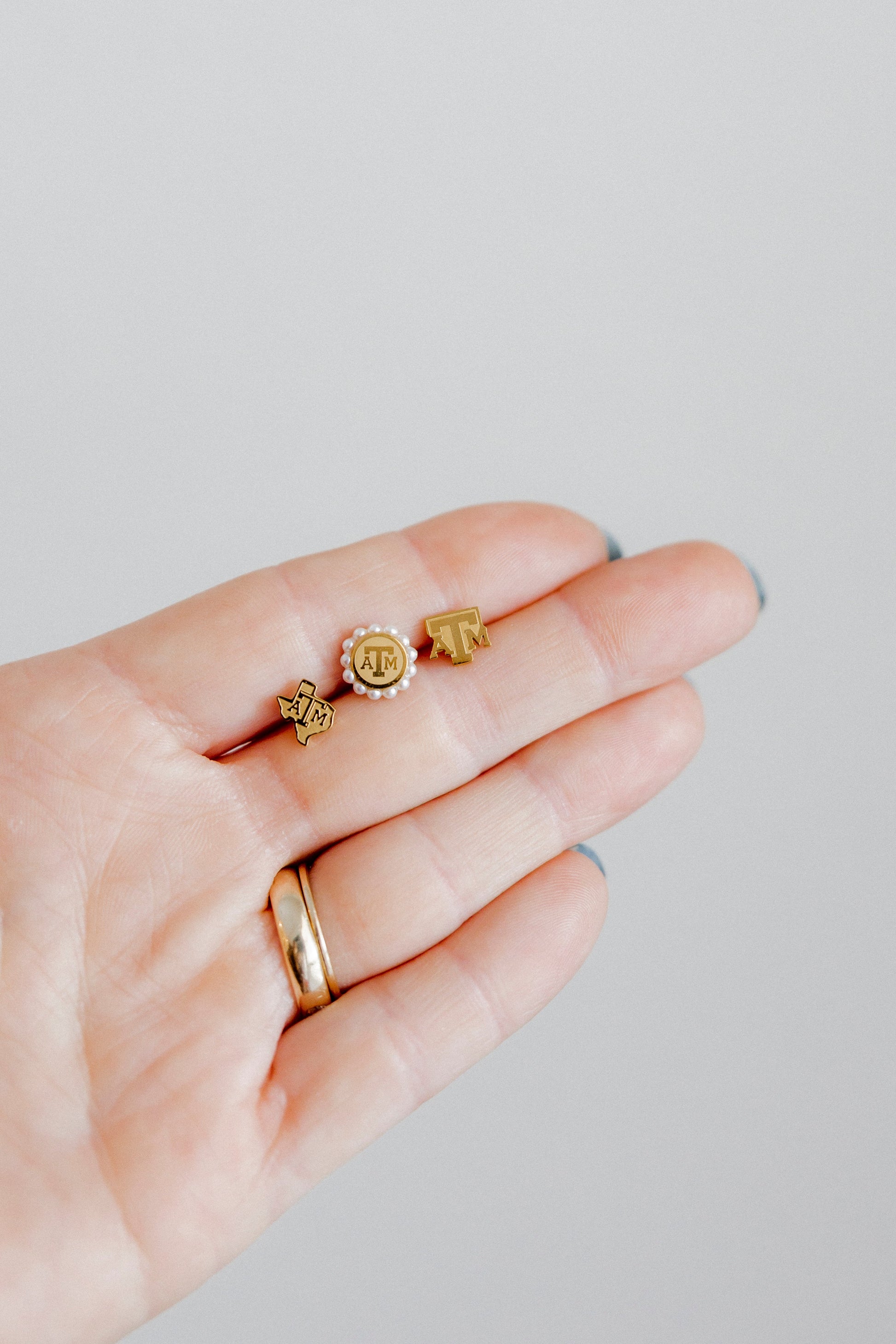 Hand wearing gold rings with small circular designs on a light gray background