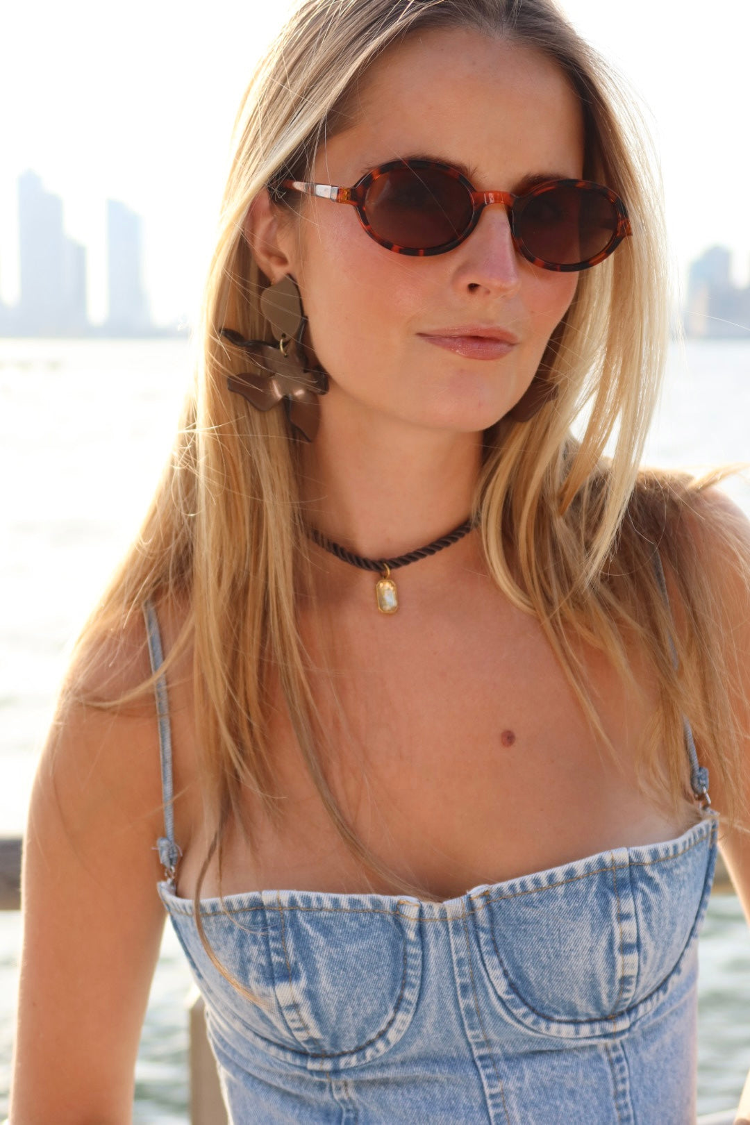 Woman wearing acetate statement earrings and a denim top with a cityscape in the background